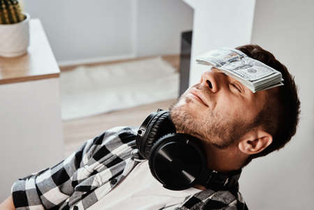 Man sleeping in workplace with stack of dollar bills on his foreheadの写真素材