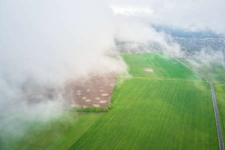 Flight through the clouds. Aerial view of green field with fluffy clouds. Nature landscape, bird eye viewの写真素材
