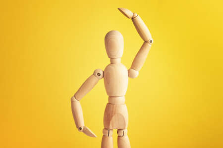 Wooden doll with gesture on yellow background. Mannequin shows gesture. Figure of wooden human with...