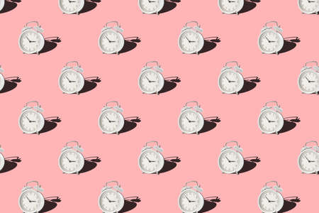 Vintage alarm clock on pink background. Seamless patern with white retro alarm clock. Minimal styleの写真素材