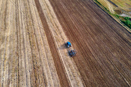 Tractor plows ground on cultivated farm field. Aerial view of tractor preparing the soil for planting cropsの写真素材