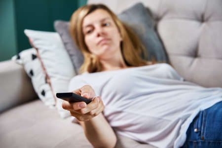 Woman resting at home. Person watch TV set while luying on the sofa and switch channels with remote controlの写真素材