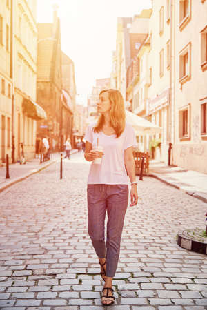 Coffee paper cup in woman hands. Woman drinks coffee to go at city street.の写真素材