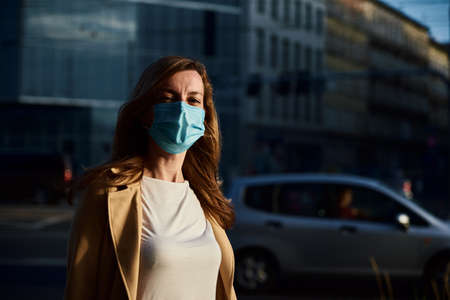 Beautiful caucasian woman wearing protective medical mask at city street. Portrait of millenial woman. Social distance and protect from coronavirusの写真素材