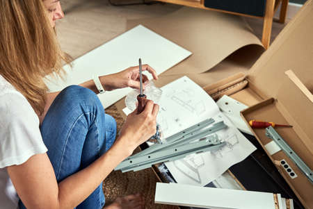 Woman reading manual instruction to assemble furniture in the living room