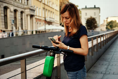 Woman unlock electric scooter for rent using mobile phone app. Modern urban eco transport