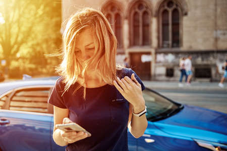 Woman and using smartphone at city street. Millennial woman walks at city with mobile phoneの写真素材