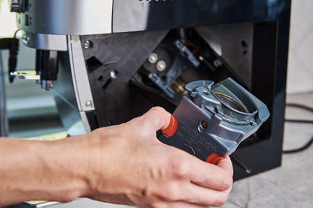 Automatic coffee machine cleaning. Woman inserts mechanism inside coffee machine. Household appliances maintenanceの写真素材