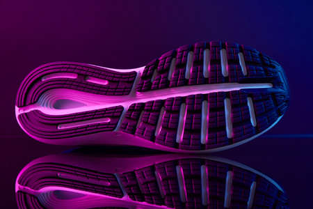 Sole of sport shoe with neon lights. Close up sneakers on dark background. Creative fashion style...