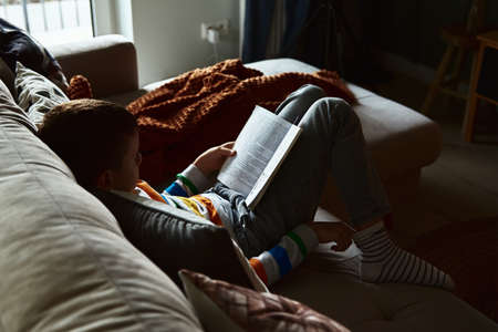 Young boy reading book on the sofa at homeの写真素材