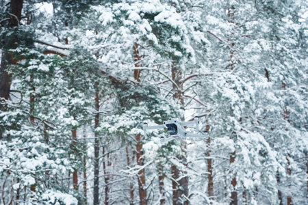 Quadcopter flying against snowy forest. Drone flight in winter