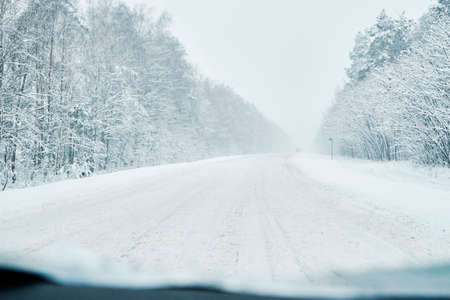 Winter forest with snowy road. Cars move on slippery road, dangerous drivingの写真素材