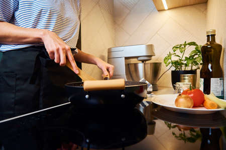 Woman cooking bolognese sauce in pan on induction stove in the kitchenの写真素材