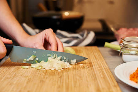 Woman with knife cuts onion on slices for cookingの写真素材