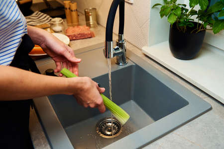 Woman prepare for cooking, wash fresh celery vegetable in kitchenの写真素材