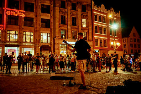 Street music performance. Man with guitar singing songs at night city street before people. Wroclaw, Poland - August 14, 2021のeditorial素材