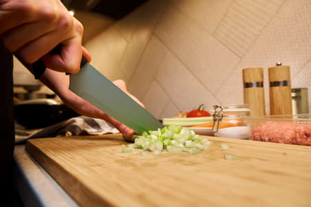Woman with knife cuts fresh celery slices for cookingの写真素材