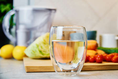 Glass of pure water, cleaning filter cartridge and fresh vegetables on tableの写真素材