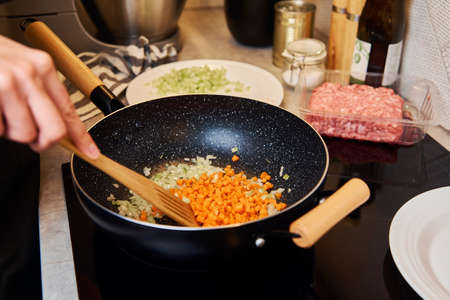 Woman cooking bolognese sauce in pan on induction stove in the kitchenの写真素材