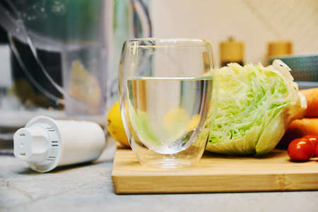 Glass of pure water, fcleaning filter cartridge and fresh vegetables on tableの写真素材