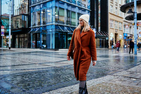 Woman in coat and eyeglasses walking at city street at rainy dayの写真素材