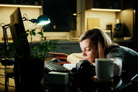 Tired woman works from home use computer at night, overwork burnout, freelancer works remote at home workplaceの写真素材