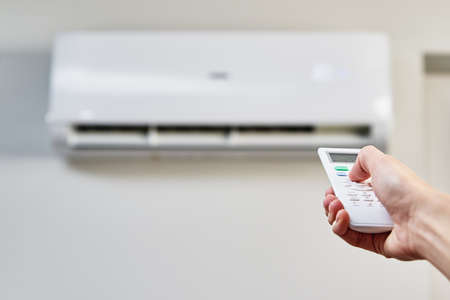 Hand adjusting temperature on air conditioner with remote control, Working air conditioner for comfort temperature in home at hot summerの写真素材