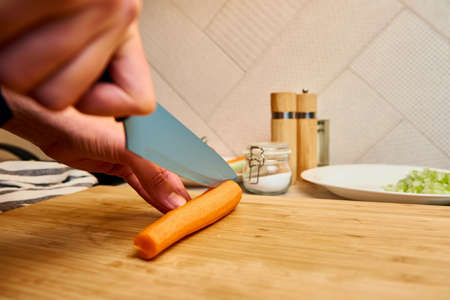 Woman chops carrot on cutting board, close up