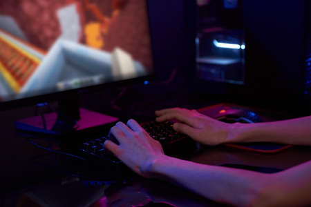Teenaeger boy play computer video game in dark room, use neon colored rgb mechanical keyboard, place...