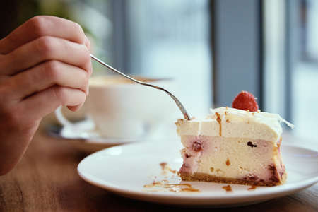 Woman eating rasberry cheesecake and drinks coffee in cafe, breakfast at public placeの写真素材