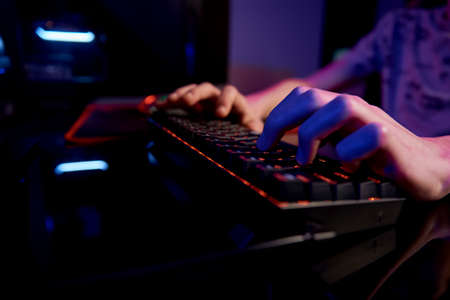 Professional gamer play computer video game in dark room, use neon colored rgb mechanical keyboard,...