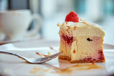 Cup of coffee and piece of raspberry cheesecake on cafe table near window, breakfast at public placeの写真素材