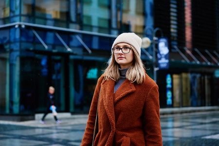 Woman in coat and eyeglasses walking at city street at rainy dayの写真素材