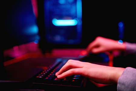 Teenager boy play computer video game in dark room, use neon colored rgb mechanical keyboard,...