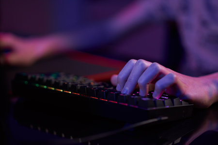 Professional gamer play computer video game in dark room, use neon colored rgb mechanical keyboard,...