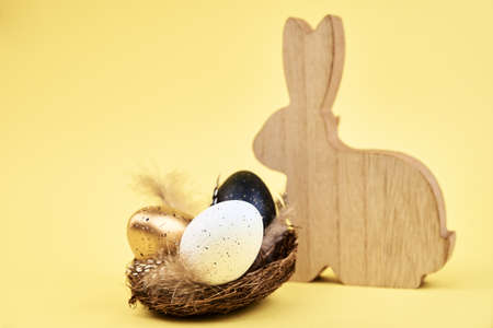 Wooden rabbit and nest with small eggs on yellow background, Happy Easter card