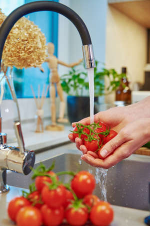 Woman wash fresh red cherry tomatos at kitchen sink, Healthy eating