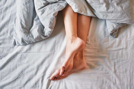 Morning concept, Woman sleeping in bed, Naked female legs under blanketの写真素材