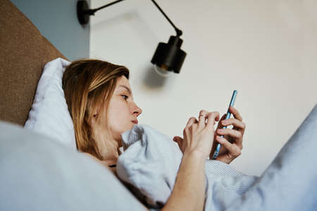 Caucasian woman relaxing in bed and use smartphone, Online communication and social media concept, Lazy weekendの写真素材