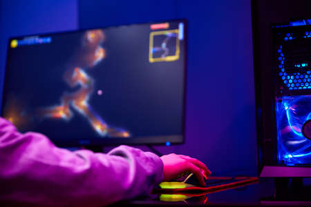 Teenager boy play computer video game in dark room, use neon colored rgb mechanical keyboard,...