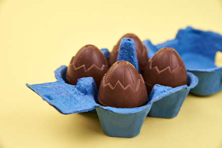 Chocolate eggs in blue box on yellow background with cope space, Happy Easter