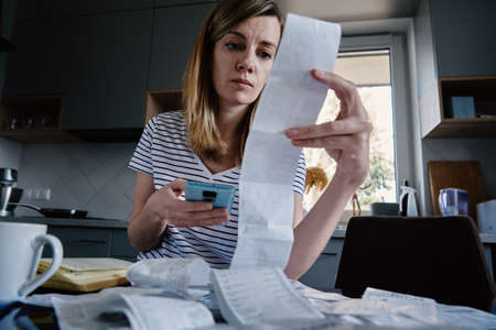 Woman looking at paper bill and counting expensesの写真素材