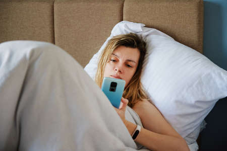 Caucasian woman relaxing in bed and use smartphone, Online communication and social media concept, Lazy weekendの写真素材
