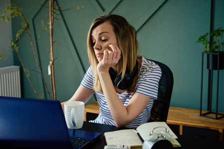 Caucasian woman sitting at table at home office and works with laptop. Freelancer remotely working