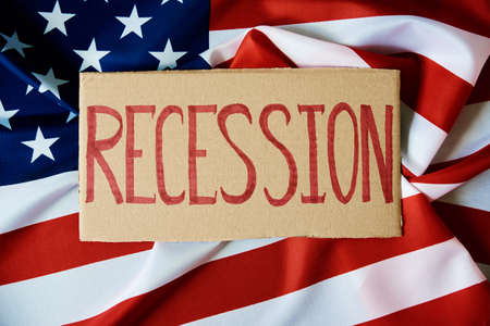Concept of recession and financial problem in USA banking system and world economic crisis,Cardboard with word recession against national american flagの写真素材