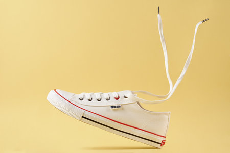 White female Big Star sneakers with flying shoe lace against yellow background, Casual trendy shoes closeup, Creative minimal design with copy space. Wroclaw, Poland - April 15, 2022のeditorial素材