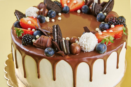 Birthday cake on yellow background. Close up of cake decorated with fresh berries and chocolate sweets on color background. Delicious dessert for partyの写真素材