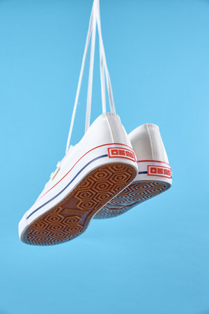 White female Big star sneakers hanging on woman hand with shoe lace against blue background, Casual...