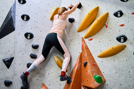 Woman climbing up on wall at bouldering gym. Female climber training, hanging on bouldering climbing wall. Active lifestyle and extreme sport concept.の写真素材