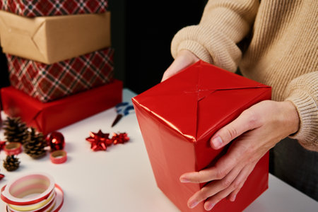 Woman in warm sweater packaging gift box with craft paper. Present for holiday event. Surprise for christmas partyの写真素材